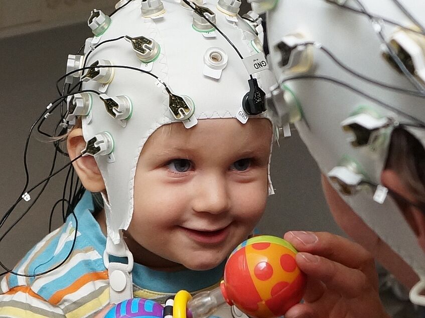 Erwachsene Person und Kind mit EEG-Kappe in Spielsituation
